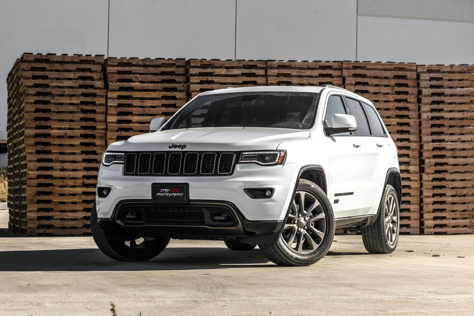 A sleek white Jeep Grand Cherokee parked in front of stacked wooden pallets, showcasing its luxury features.